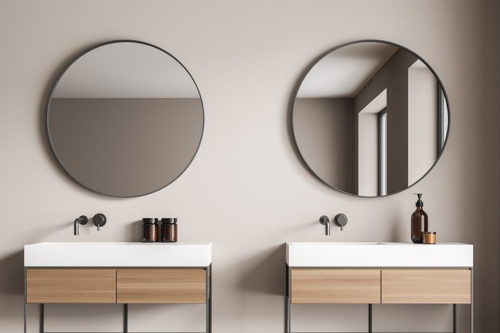 Beige bathroom wall with two stylish round mirrors over the two vanities. Elegant design with a concept of a modern on trend interior. 3d rendering