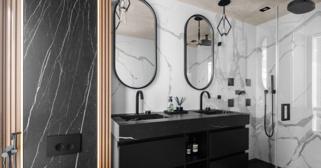 Luxury Klein Kitchen and Bath bathroom renovation with black double vanity, marble-look walls, glass shower, and matte black fixtures