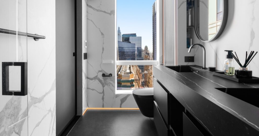 Klein Kitchen and Bath luxury bathroom renovation featuring a black double vanity, marble-look porcelain walls, walk-in shower, and Manhattan skyline views
