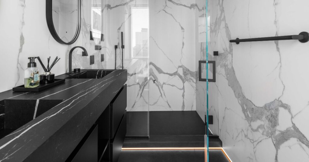 Luxury NYC bathroom renovation with black stone vanity, frameless glass shower, marble-look porcelain walls, and matte black fixtures
