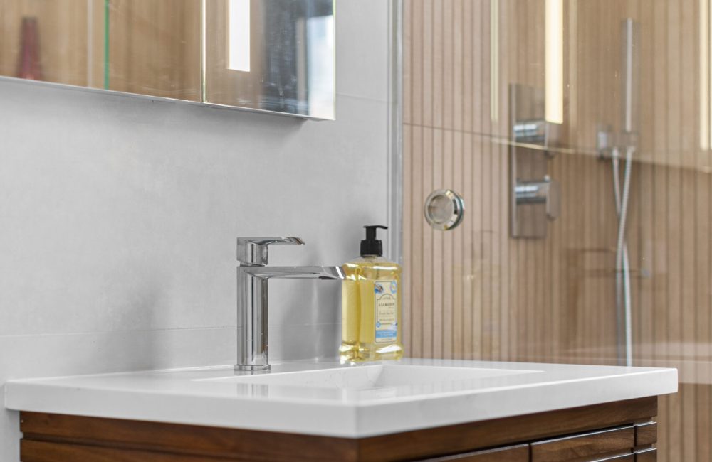 MA_448056_1 Modern bathroom makeover in NYC with a wood-accented shower, floating vanity, and sleek LED lighting.
