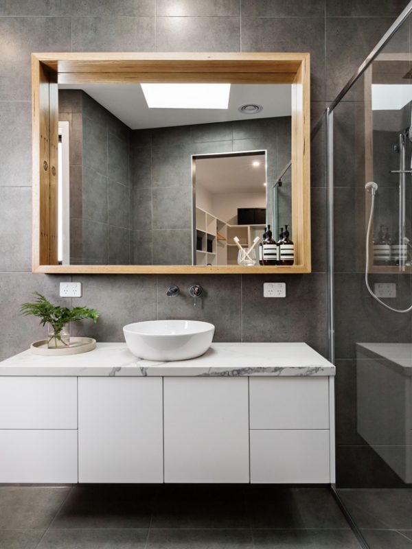Modern bathroom with a floating vanity, vessel sink, large framed mirror, and a glass-enclosed walk-in shower featuring dark porcelain tiles and a herringbone accent wall